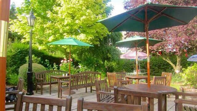 Outdoor seating area with wooden tables and benches, green umbrellas, and lush greenery in a tranquil setting.