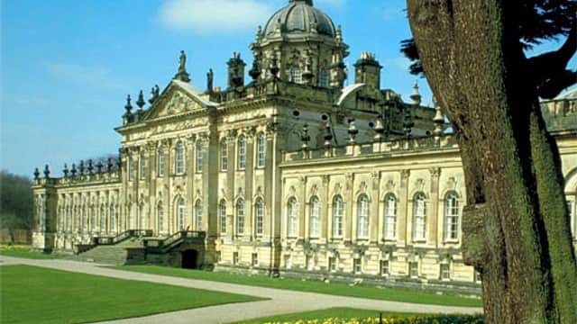Historic building with ornate architecture, surrounded by lush greenery and blooming daffodils under a clear blue sky.