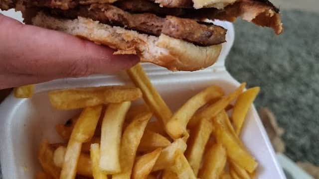 A hand holds a half-eaten burger next to a container of golden fries on a textured surface.