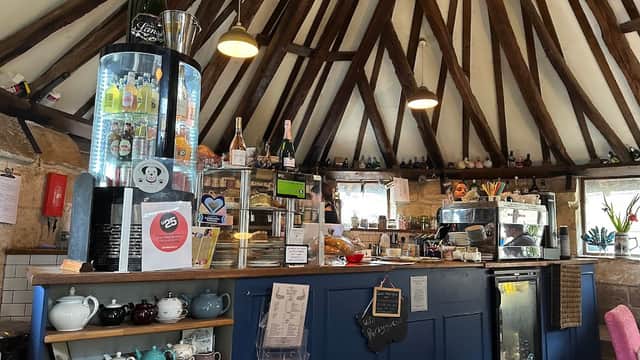 Cozy cafe interior with wooden beams, a blue counter, display of drinks, and various teapots on shelves.
