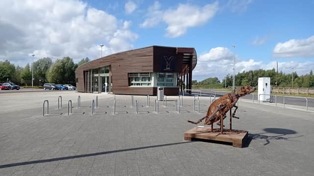 Modern building with large windows, a metal sculpture of a dog, and parking spaces under a blue sky with clouds.
