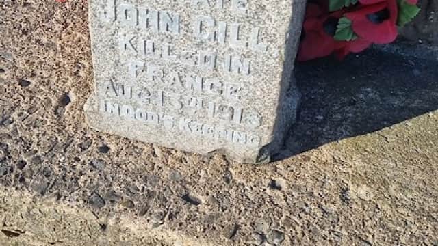 Stone memorial with engraved text surrounded by red poppies and wooden crosses on a nature trail.