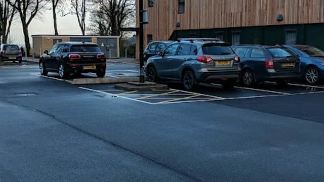Pay & Display parking area with parked cars, trees in the background, and a modern wooden building.