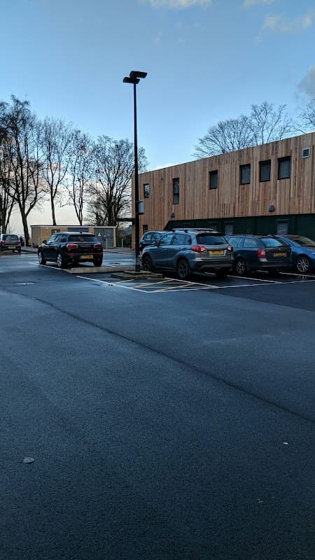 Pay & Display parking area with parked cars, trees in the background, and a modern wooden building.