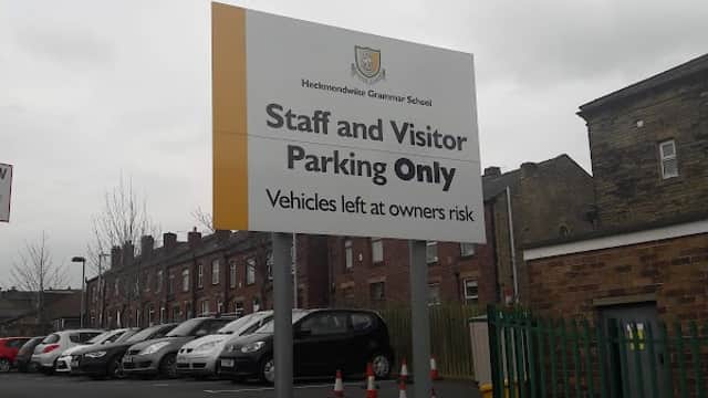 Sign for "Staff and Visitor Parking Only" at Heckmondwike Grammar School, with a view of the car park and buildings.