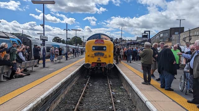 Yellow train at Scarborough Station, with crowds of people on the platform and clear blue skies above.