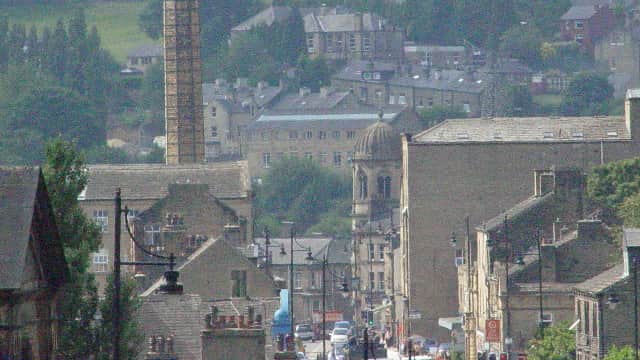 View of Riverside Garage in Luddenden, with surrounding buildings and a hilly landscape in the background.