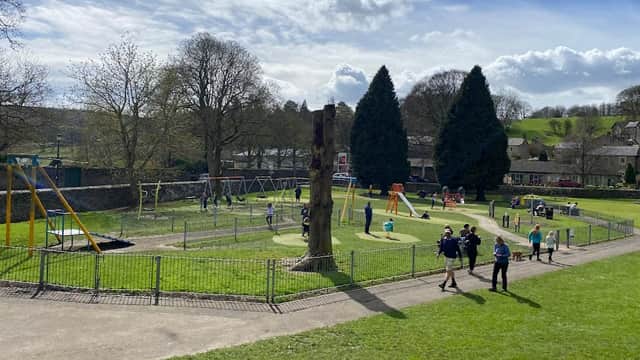 Playground with swings, climbing structures, and children playing on grass, surrounded by trees and a stone wall.