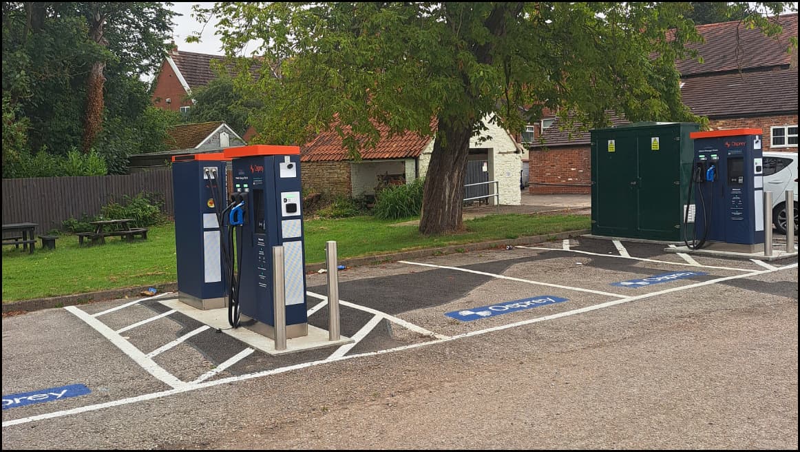 Osprey Charging Station with multiple EV chargers and a green utility box in a parking area, surrounded by trees.