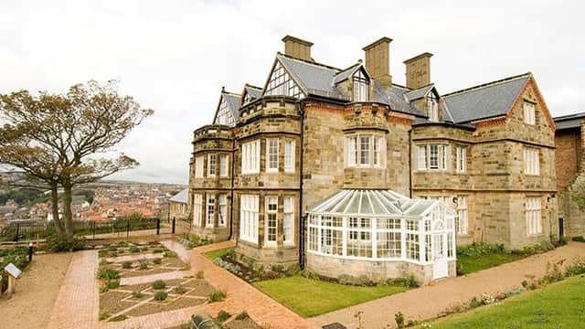 Victorian-style hotel with a glass conservatory, surrounded by gardens and overlooking a scenic view of Whitby.