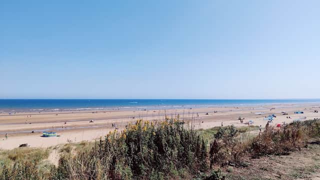 Expansive sandy beach with people enjoying the sun, colorful umbrellas, and a clear blue sky over the sea.