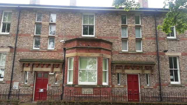 Victorian-style brick building with red doors, large windows, and a decorative entrance in a tree-lined setting.