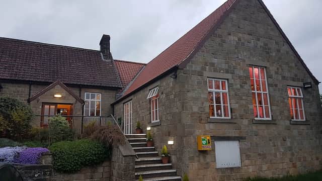 Stone building with red roof, steps leading to entrance, and colorful flowers in front, under a cloudy sky.