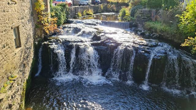 A serene waterfall cascades over rocks, surrounded by stone buildings and greenery in Hawes, Yorkshire.