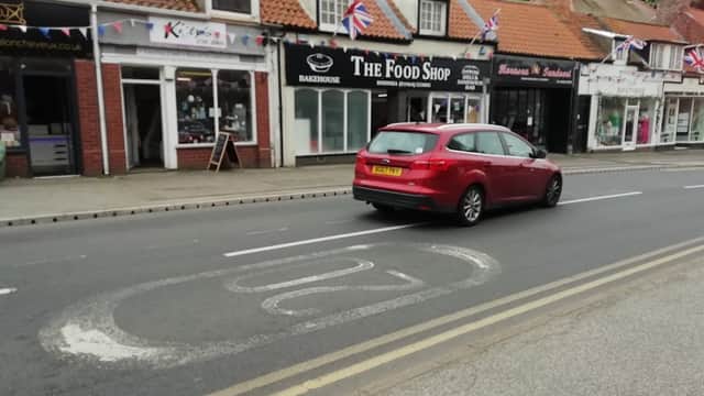 On-street parking area with a red car, shops with Union Jack flags, and a clear road in Hornsea, Yorkshire.