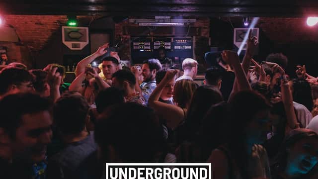 Crowded nightclub scene with people dancing and a DJ in the background, vibrant lights illuminating the atmosphere.