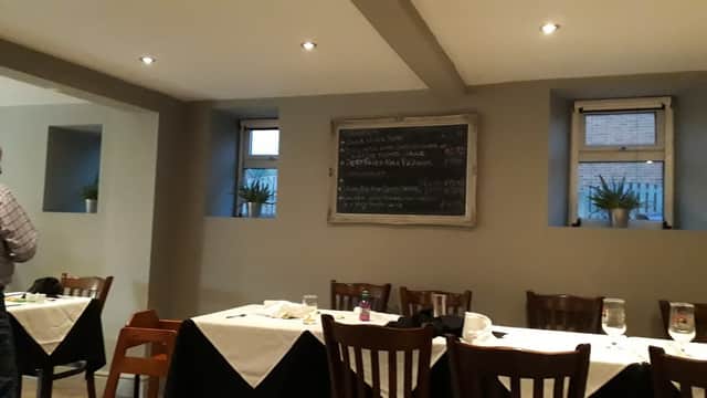 Interior of La Anchor with wooden tables, a chalkboard menu, and potted plants by the windows.