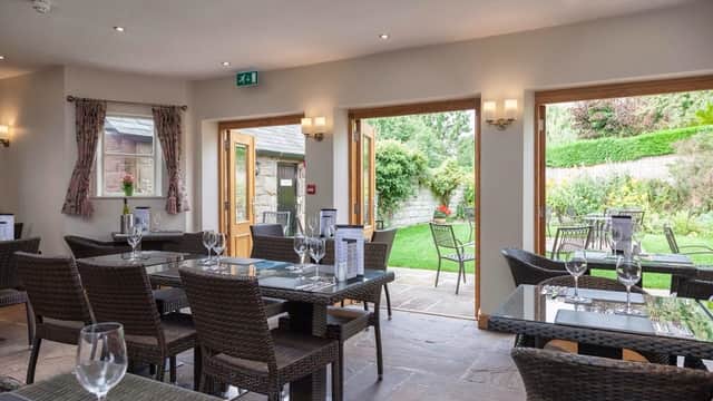 Cozy bar interior with tables set for dining, large windows opening to a lush garden area.