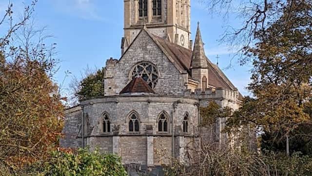 St Helen's Church features a tall tower, ornate stonework, and surrounded by trees and greenery under a blue sky.