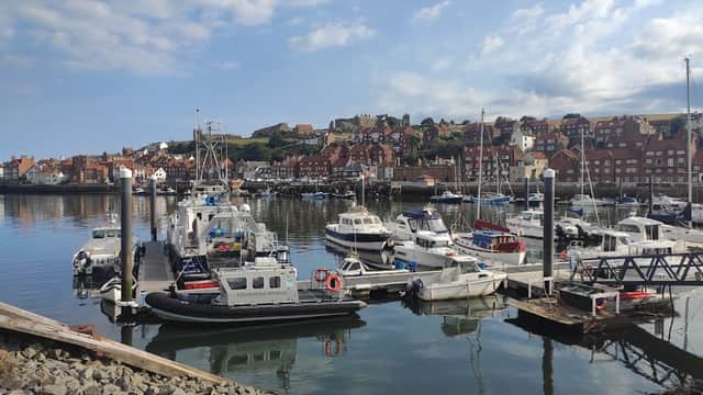 Pay & Display parking sign with boats and a scenic harbor view in Whitby, Yorkshire, under a partly cloudy sky.