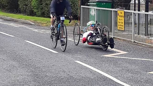 Cyclists on a road near Chapel Haddlesey Church of England Primary School, with greenery and a school sign in view.