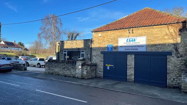 Central Garage Welburn Ltd building with stone walls, blue garage doors, and a sign on a clear, sunny day.