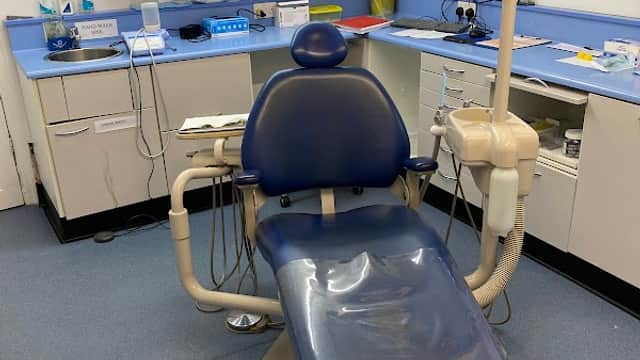Dental chair in a clean clinic with cabinets, equipment, and a computer workstation in a well-lit room.