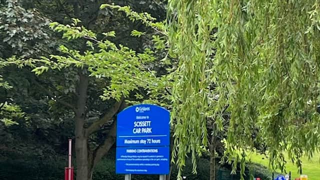 Free parking sign at Wakefield Road, Clayton West, with parked cars and trees in the background.