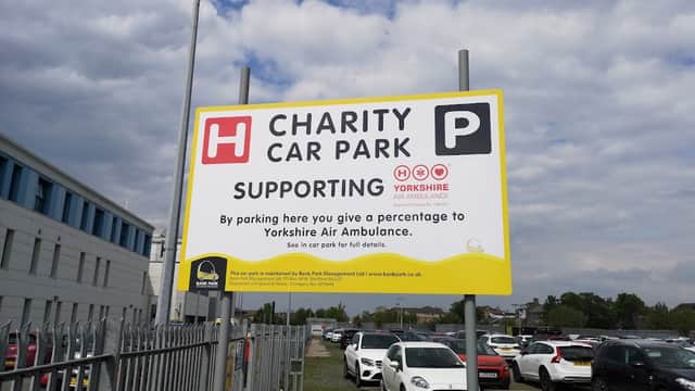 Sign for Charity Car Park supporting Yorkshire Air Ambulance, with parked cars and a cloudy sky in the background.