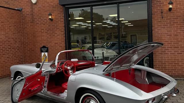 Silver retro classic car with red interior parked outside a shop, featuring a sign that reads "RETRO CLASSIC GARAGE."