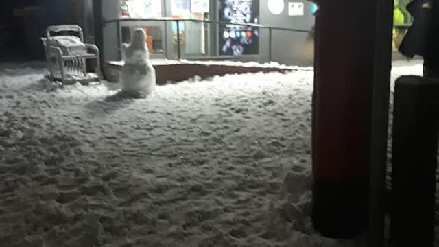 Co-op store entrance with snow-covered ground, a snowman, and a red post box at night.