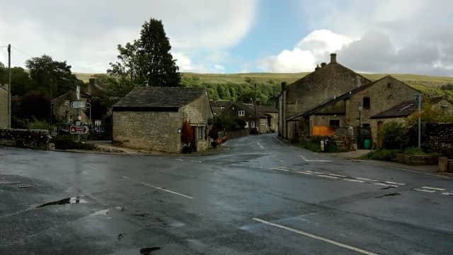 A quiet village street in Kettlewell, Yorkshire, with stone buildings, a tree, and a cloudy sky.