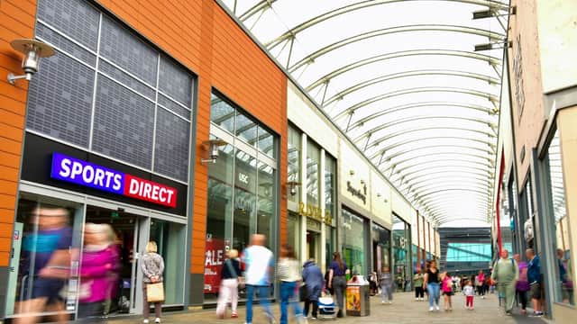 Busy shopping arcade with a Sports Direct store, modern architecture, and shoppers walking under a curved glass roof.