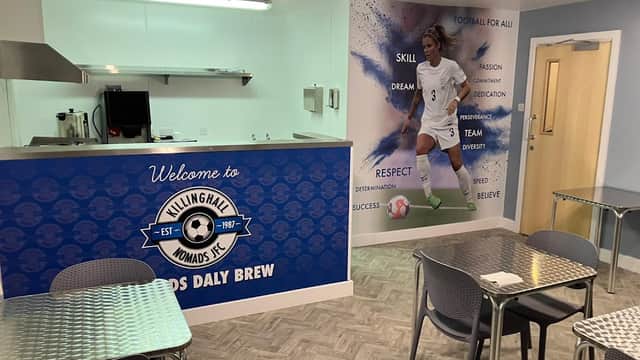 Bright cafΓ© interior with metal tables, a welcoming sign, and a mural of a female soccer player on the wall.