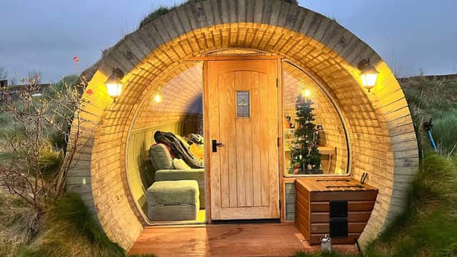 Cozy round cabin with a wooden door, soft seating, and decorative lights, surrounded by grassy landscape.