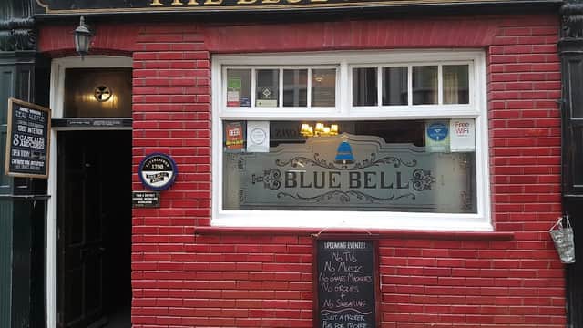 Traditional pub exterior with red brick, large window displaying "The Blue Bell," and a chalkboard menu outside.