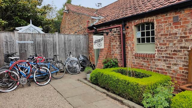 Bicycles parked outside a rustic brick building with a sign for "Twisted Cogs" and neatly trimmed hedges.