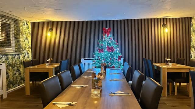 Cozy dining area with wooden tables, black chairs, and a decorated Christmas tree in the corner.