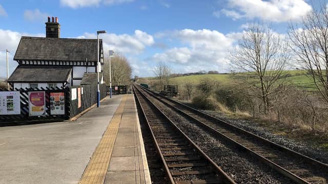 Railway tracks stretching into the distance beside a quaint station building under a blue sky with scattered clouds.