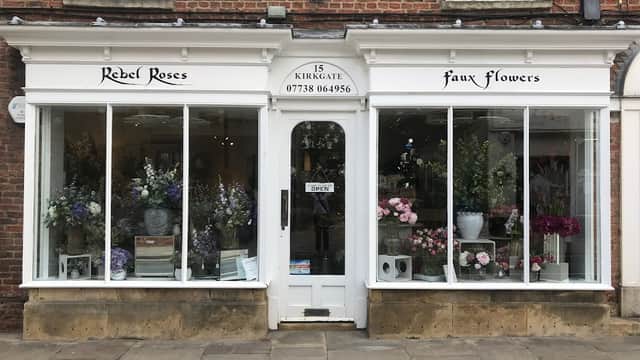 Shopfront of Rebel Roses, featuring large windows displaying colorful silk flowers and floral arrangements.