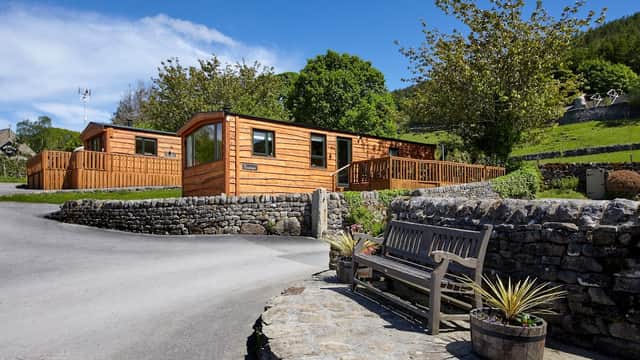 Wooden lodges with decking surrounded by greenery, stone walls, and a bench in a scenic Yorkshire park.