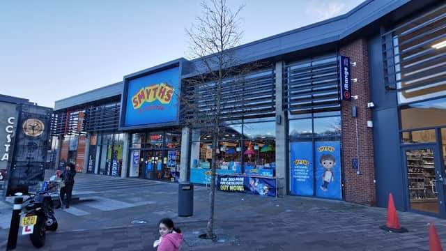 Smyths Toys Superstore entrance with colorful signage, large windows, and a child walking by on the plaza.