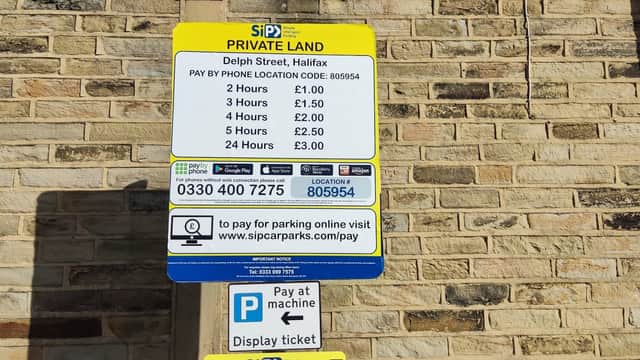 Sign detailing parking rates and payment options at Delph Street car park, with a stone wall background.