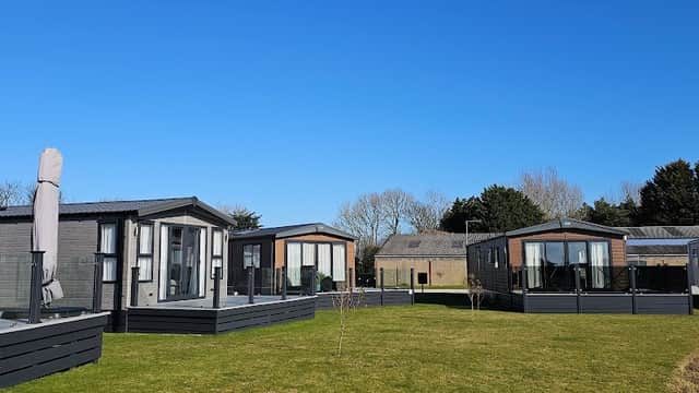 Modern lodges with glass balconies set on a green lawn under a clear blue sky at Maples Country Park, Atwick.
