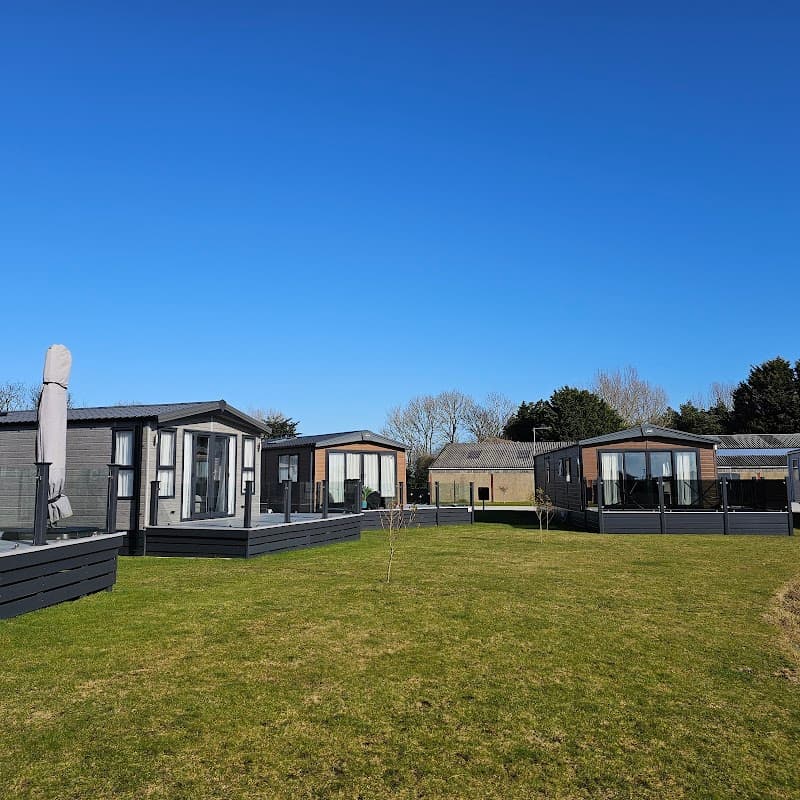 Modern lodges with glass balconies set on a green lawn under a clear blue sky at Maples Country Park, Atwick.