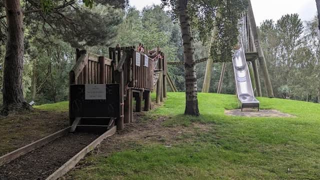Wooden playground structure with slide, surrounded by trees and grassy area at Playworld, Kinsley, Yorkshire.