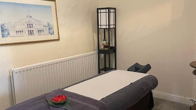 Massage table with towels, decorative flower, and a framed artwork in a cozy treatment room.