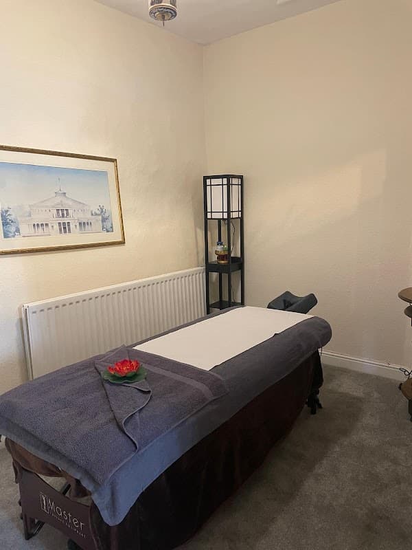 Massage table with towels, decorative flower, and a framed artwork in a cozy treatment room.