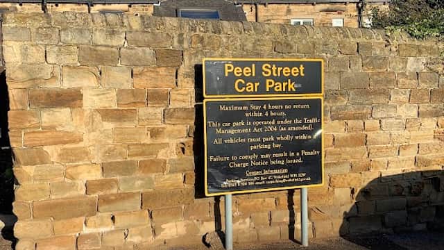Sign for Peel Street Car Park with stone wall background, detailing parking rules and payment instructions.