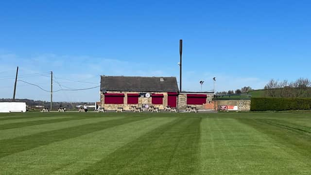 Kirkheaton Cricket and Bowling Club with a well-maintained green field and a brick building under a clear blue sky.